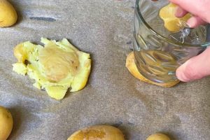 abgekuehlte gekochte kartoffeln auf einem mit backpapier ausgelegten backblech mit einem gals platt druecken