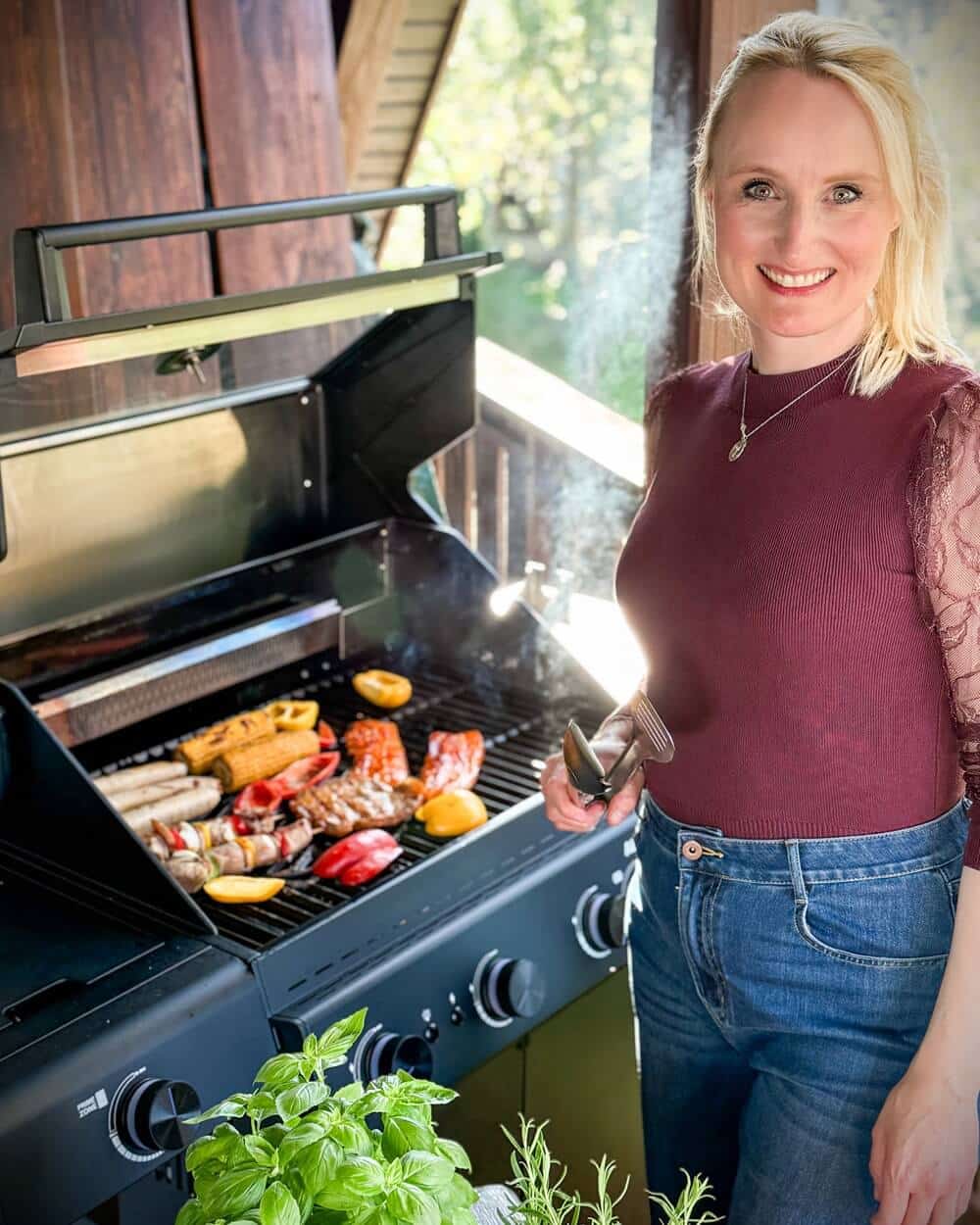 Anja auf dem Balkon, begruesst mit einem Lächeln die Besucher, vor ihr Gemüse und Fleisch auf dem Grill