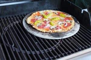gebackene pizza auf pizzastein im gasgrill - die frau am grill
