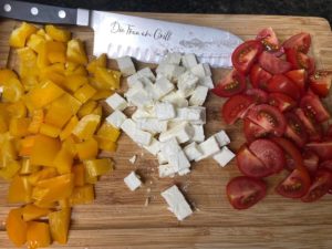 gelbe paprika, cocktailtomaten und feta klein geschnitten auf einem brett