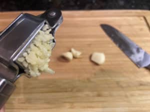 geschaelte knoblauchzehen durch knoblauchpresse gedrueckt