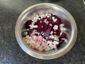 in scheiben geschnittene gekochte rote beet mit zwiebelwuerfel in einer salatschuessel