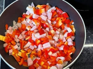 klein geschnittene paprika mit zwiebeln und schinkenwuerfeln in einer pfanne