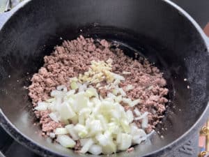 klein geschnittene zwiebeln und gehackten knoblauch zu kruemelig gebratenem hackfleisch geben