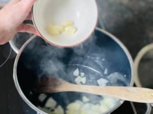 knoblauch zu angeduensteten zwiebeln in topf geben