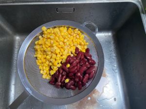mais und kidneybohnen im sieb ueber dem spuelbecken abgegossen