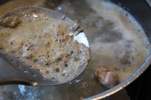 mit der schaumkelle den Schaum bei der Bruehe entfernen - die frau am grill