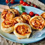 Fertig gebackene Pizzaschnecken liegen appetitlich angerichtet auf einem Teller.