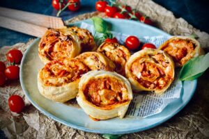 Fertig gebackene Pizzaschnecken liegen appetitlich angerichtet auf einem Teller.